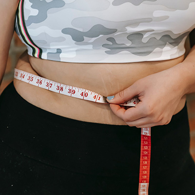 A woman in fitness attire wrapping a measuring tape around her waist